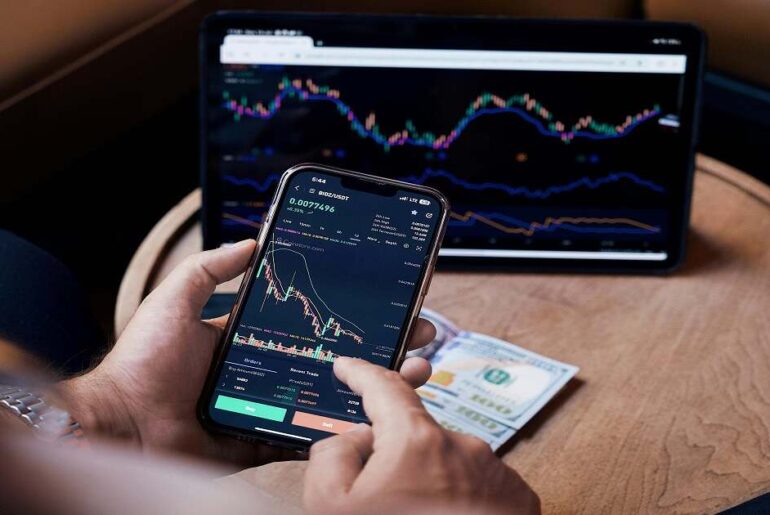 Trader analyzing live margin trading charts on a smartphone with a laptop displaying market data, highlighting key trends and performance in margin trading.