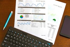 Analytics report on paper with graphs and pie charts showing marketing performance, a keyboard, and a pen, illustrating data-driven marketing tips.