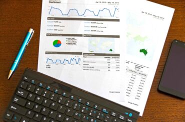 Analytics report on paper with graphs and pie charts showing marketing performance, a keyboard, and a pen, illustrating data-driven marketing tips.