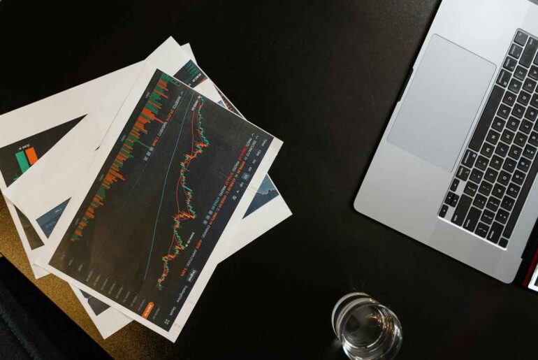 Trading for Penny Stocks - A close-up view of a laptop and printed stock charts, showing candlestick patterns