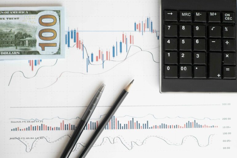 a calculator, a $100 bill, and trading charts with indicators, symbolizing the use of leverage in trading to maximize potential returns