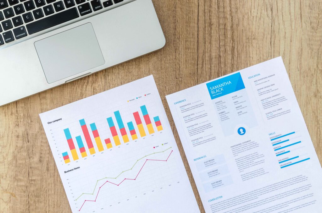 Marketing tips for startups: A close-up of a laptop, colorful charts, and a sample resume on a wooden desk, highlighting career growth and analysis.